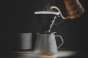 Steam rising as hot water is poured over fresh grounds in a black pour-over dripper, coffee blooming into a glass carafe. Photo by Julien Labelle.